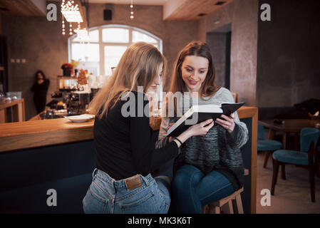 Two Girl`s absorbed in reading book during the break in cafe. Cute lovely young women are reading book and drinking coffee Stock Photo